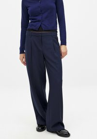 Navy wide-leg trousers with pleats, made of smooth fabric. Paired with a dark blue long-sleeve cardigan and glossy black shoes.