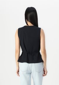 Black sleeveless top with a fitted bodice, peplum hem, and a tie detail at the waist; worn with light blue jeans. Smooth fabric texture.