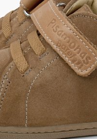 Zapatos de ante marrón con superficie texturizada, que cuentan con una correa de cuero color beige y cordones beiges. Detalle de costura notable a lo largo del costado.