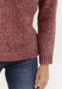 Adīts džemperis mīkstā, tekstūrētā rozā krāsā ar daudzkrāsainiem punktiņiem. Ribota apkakle un apakšmalē, saskaņots ar tumšām džinsu biksēm.