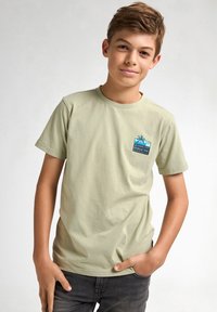 Lichtgroen katoenen T-shirt met korte mouwen, met een kleine blauwe grafiek van een palmboom en zonsondergang op het linker borstzak gebied.