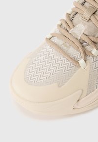 Beige sneakers med ovandel i mesh med ett sicksackmönster, vadderad tunga och snörning. Slät gummisula med texturerade detaljer.