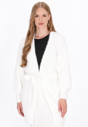 Weißer Strickcardigan mit langen Ärmeln, offener Front und Krawatte in der Taille; weiche Textur mit flauschigem Finish; kombiniert mit einem schwarzen Oberteil darunter.