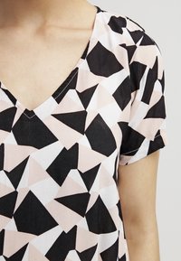 V-ringad blus med ett geometriskt mönster i svart, vitt och blekrosa. Korta ärmar och lätt, strukturerad tyg.