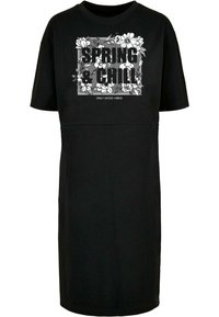 Svart bomullsdrakt med korte ermer og løs passform. Har hvit blomstergrafikk med teksten "SPRING & CHILL" i midten.
