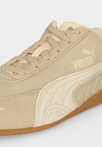Μπεζ σουεντ αθλητικό Puma με κρεμ λεπτομέρεια από σουεντ ριγέ και ελαστική σόλα από καουτσούκ, με μπεζ κορδόνια και λογότυπο Puma στο πλάι.
