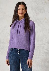 Lila gestrickter Kapuzenpullover mit gerippter Textur, Kordelzugverschluss und langen Ärmeln, kombiniert mit dunklen Jeans aus Denim mit Knopfdetails.