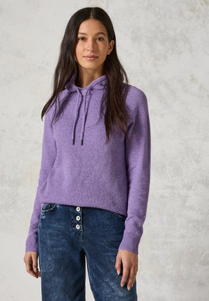 Lila gestrickter Kapuzenpullover mit gerippter Textur, Kordelzugverschluss und langen Ärmeln, kombiniert mit dunklen Jeans aus Denim mit Knopfdetails.