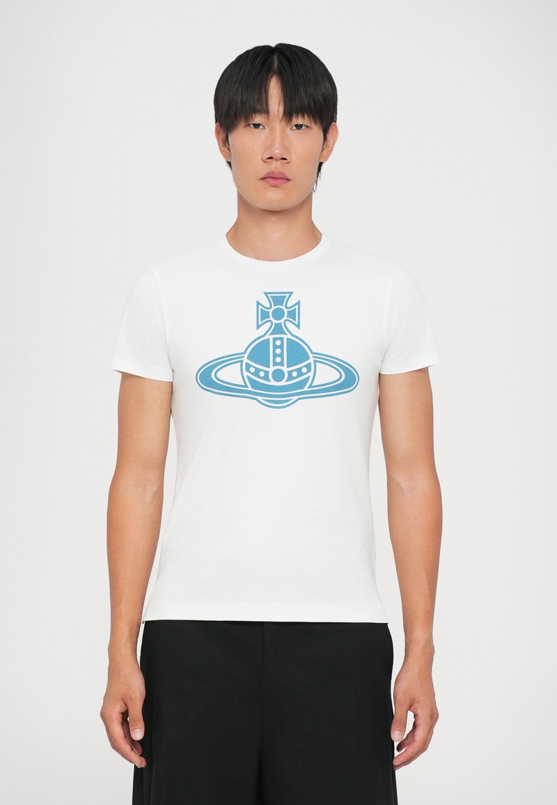 T-shirt en coton blanc avec un design graphique bleu d'une planète avec une croix et des anneaux, à manches courtes et col rond.