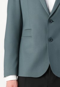 Blazer verde acqua con rever a doppio petto, due bottoni e una vestibilità su misura. Caratterizzato da una texture liscia e da una tasca singola sul petto.