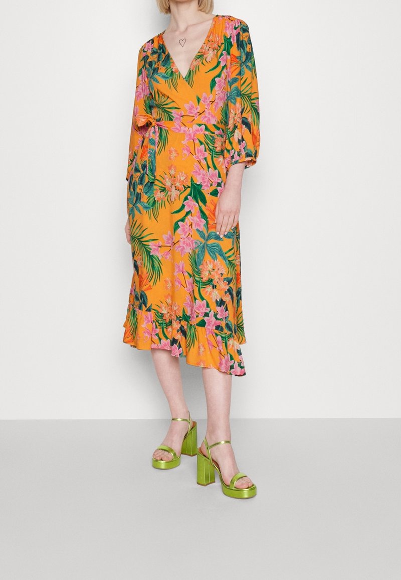 Kwiatowa sukienka midi w intensywnym pomarańczowym kolorze, z różowymi kwiatami i zielonymi liśćmi. Dekolt w kształcie litery V, rękawy o długości trzy czwarte oraz falbaniasty dół.