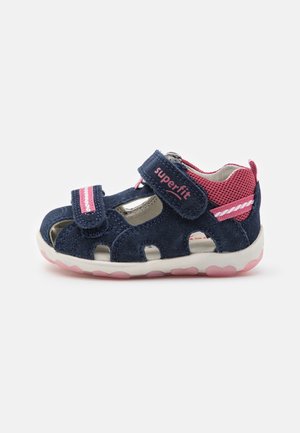 Sandale pour tout-petit bleu marine et rose avec des brides Velcro ajustables, un dos en mesh respirant, une semelle rembourrée et une semelle extérieure blanche avec semelle en forme de cœur rose.