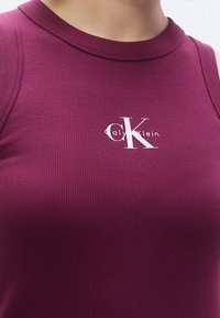 Burgunderrotes, geripptes Tanktop mit rundem Ausschnitt, vorne mit weißem CK-Logo und einem figurbetonten Design, das die Struktur betont.