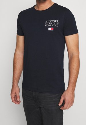 T-shirt a maniche corte blu navy in cotone, con scritte bianche e una piccola grafica di una bandiera sul petto a sinistra. Vestibilità standard.