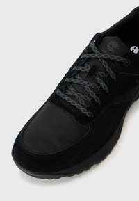 Črne teniske iz semiša in mrežaste tkanine, z okroglo konico, teksturirano zgornji del in sivo vezanje s pisanjem. Timberland logo na ježku.