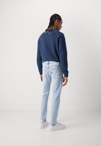 Pull navy avec des poignets côtelés, associé à un jean droit bleu clair avec poches avant et arrière, porté avec des baskets blanches.