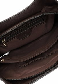 Interior de un bolso de cuero marrón con dos compartimentos con cremallera, forro de tela suave y un acento de cuero de marca en el bolsillo.