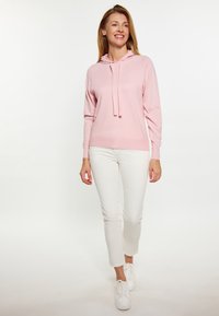 Hanorac cu glugă de culoare roz deschis, cu mâneci lungi și șnururi, asortat cu pantaloni albi slim-fit și adidași albi. Design simplu și casual.