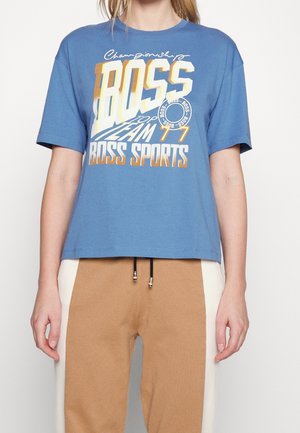 Camiseta de algodón azul con mangas cortas, que presenta un destacado texto gráfico en blanco y dorado "BOSS TEAM 77" y un cuello redondo. Diseño recortado.