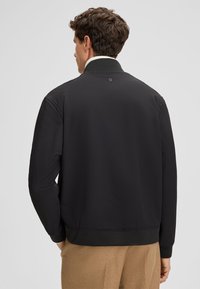 Zwarte geribde jas met een hoge kraag, elastische manchetten en zoom. Beschikt over een klein logo-detail aan de achterkant van de halslijn.