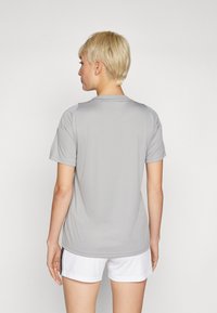 Grå treningstrøye med korte ermer, glatt tekstur, rund hals og subtile skulderdetaljer, sammen med hvite shorts.