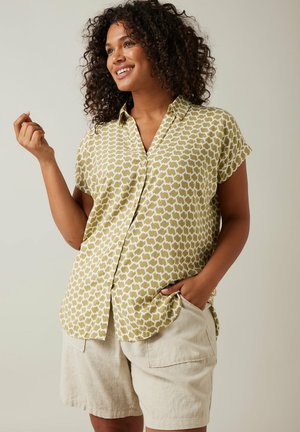 Camisa de manga corta con un patrón geométrico verde, con botones en la parte delantera y tejido suave. Combinada con pantalones cortos de lino beige, que cuentan con bolsillos laterales.