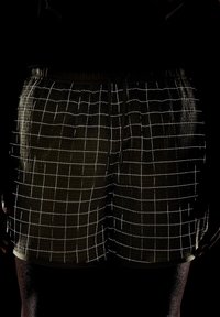 Gaiši zaļi šorti no viegla auduma, kuriem ir režģa raksts ar baltām līnijām. Jostasvieta ir elastīga, un tai ir auklas pielāgošanai.