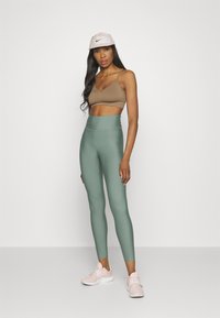 Brun sportbh, högmidjade olivgröna leggings och ljusrosa sneakers. Har justerbara axelband och en logokaps. Slät, elastisk material.