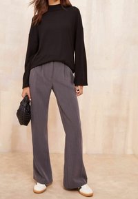 Mustat pitkät hihatoppi yhdistettynä vaaleanharmaisiin leveälahkeisiin housuihin, tekstiilissä on texturea, ja valkoisiin lenkkareihin. Asusteina on pieni musta kudottu käsilaukku.