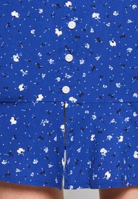 Abito floreale blu con bottoni frontali, caratterizzato da motivi di fiori bianchi e neri e una piccola fessura all'orlo, realizzato in tessuto morbido.