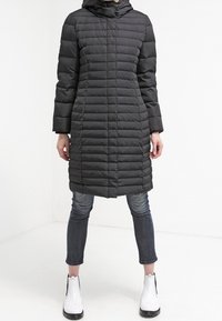 Quilted black puffer coat with a hood, featuring long sleeves and a straight cut. Paired with dark jeans and white ankle boots.