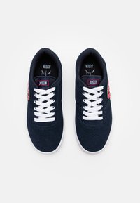 Marina mockasiner i mocka med vita snören och sålar. Har en röd och vit logotyp på sidan och perforerade detaljer på tån.