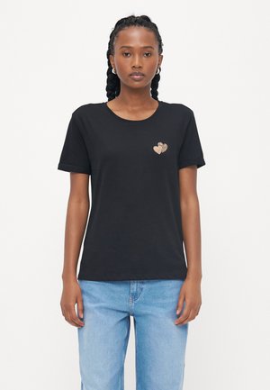 Black cotton t-shirt with short sleeves, round neckline, and a gold sequin heart design on the left chest. Worn with light blue jeans.