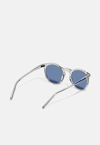 Lunettes de soleil rondes avec une monture transparente, des verres bleus et des branches claires fines. Remarquables par leur design minimaliste et leur contraste de couleurs.
