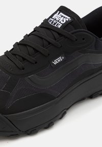 Baskets Vans MTE noires avec semelle épaisse, tige en mesh et daim, lacets noirs et logo Vans sur la languette et le panneau latéral.