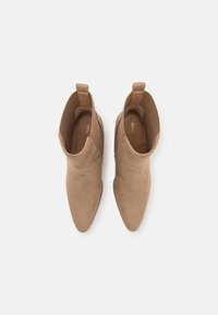 Bottes en suède beige à la cheville avec des bouts pointus, des côtés élastiques et des languettes. Texture lisse et design simple sans motifs supplémentaires.