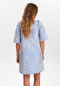 Lichtblauwe en witte jurk met bloemenpatroon. Heeft korte, opgeblazen mouwen en een losse pasvorm, gemaakt van een gestructureerde stof.