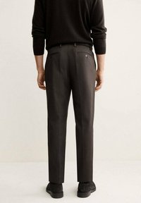 Pantalon gris foncé avec une coupe ajustée, doté d'une texture lisse, de deux poches arrière et de subtils détails de boutons, associé à un pull noir.