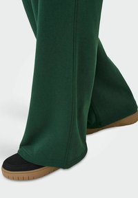 Grønne sweats med en løs pasform, der har sidesyninger og en glat tekstur, parret med sorte sneakers og en brun sål.