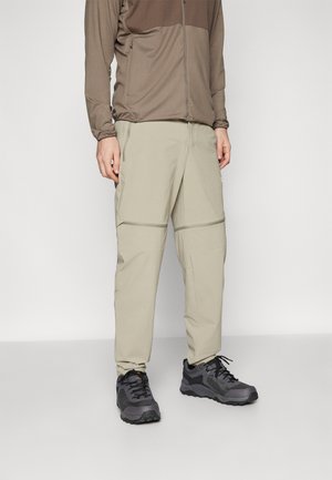 Beige, lightweight, zip-off pants with a relaxed fit; paired with dark gray hiking shoes featuring black accents and textured soles.