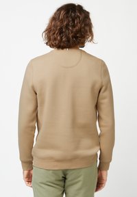 Felpa beige con collo rotondo, polsini e orlo a coste, texture liscia e dettaglio circolare sul retro, abbinata a pantaloni verde chiaro.