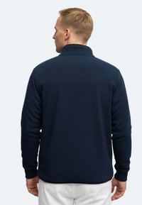 Pullover in fleece blu navy con colletto alto, superficie testurizzata e maniche lunghe; presenta polsini elasticizzati e un design slim fit.