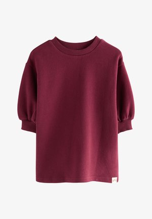 Bluza dla dziecka w kolorze bordowym z prążkowanym okrągłym dekoltem i mankietami, z lekko bufkami na rękawach o długości do łokcia oraz małą metką na dole.