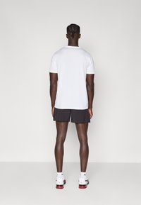 Hvit kortermet t-skjorte, svarte treningsshorts og hvite sneakers med røde detaljer. Rent design, medium passform, jevn tekstur.