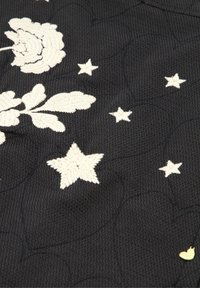 Zwarte textuurstof met witte geborduurde rozen en sterren. Een klein gouden hartaccent is ook zichtbaar in de rechterbenedenhoek.