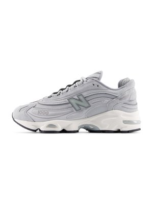 Gray athletic shoe with a suede and mesh upper, textured design, black outsole, reflective accents, and a prominent “N” logo on the side.