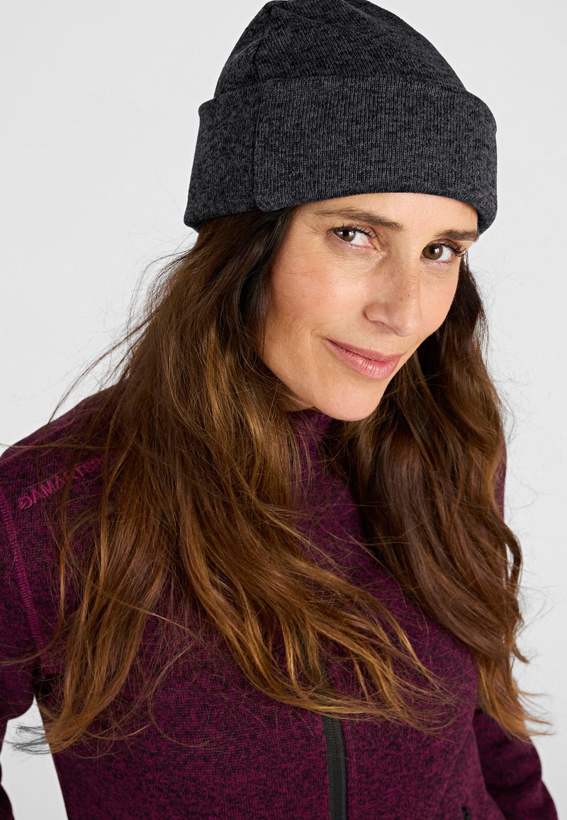 Gorro de punto gris con puño doblado, tela texturizada y un diseño ajustado. Se lleva con una chaqueta de cremallera morada oscura.