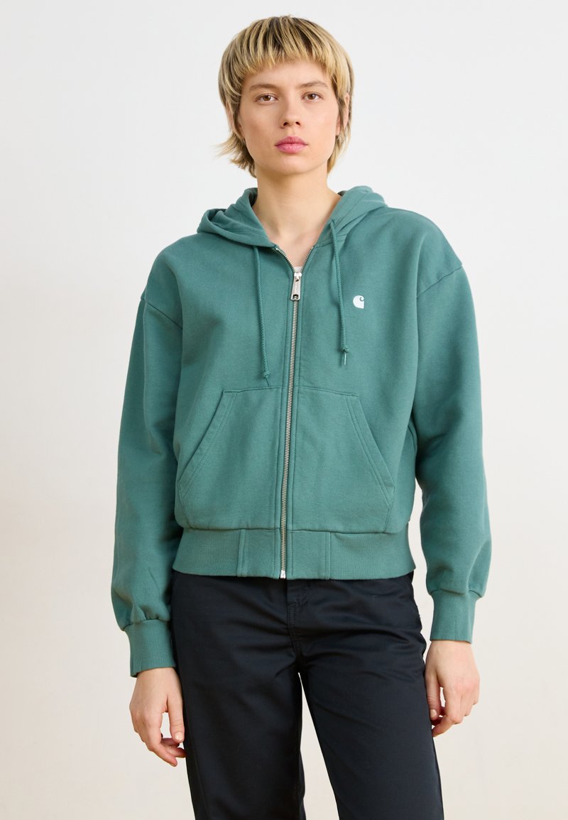 Grønn zip-up hettegenser laget av mykt stoff med kengurulomme, snorer på hetten og en liten logo på brystet.