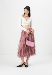 Haut-crop blanc à côtes, jupe en tulle rose superposée, escarpins noirs à bout pointu et un petit sac à main rose avec une surface texturée.