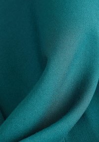 Tyrkysová látka hladkého povrchu s jemným leskem, elegantně se skládá do měkkých záhybů. Má jemný tkaný vzor.